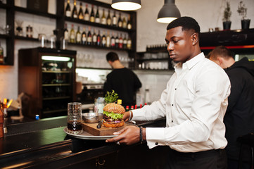 Young african american waiter man hold tray with burger at bar of restaurant.