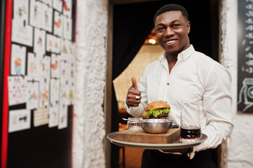 Young african american waiter man hold tray with burger at restaurant and show thumb up.