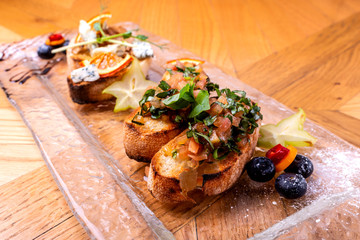 Tasty savory tomato Italian appetizers, or bruschetta, on slices of toasted baguette garnished with basil, close up on a wooden table.