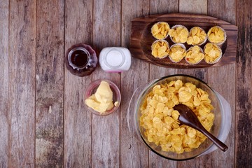 Bowl with cornflakes, conflakes cup, suger, butter and honey on  wooden background