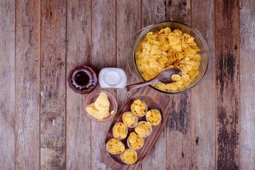 Bowl with cornflakes, conflakes cup, suger, butter and honey on  wooden background