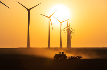 A tractor cultivating farmland during sunset at a row of windturbines. Groningen, Holland.