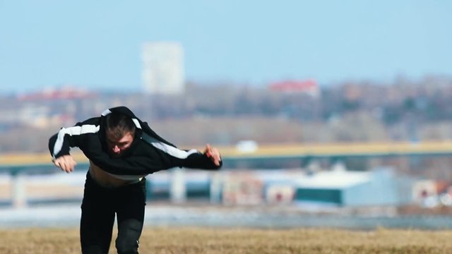 Young man doing acrobatic tricks on a grass. Urban background