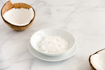 Fototapeta na wymiar Coconut Halves and Grated Coconut in a Bowl on White Marble