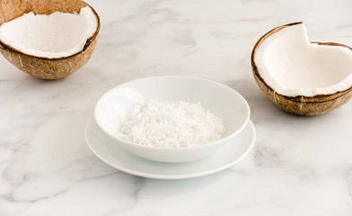 Fototapeta na wymiar Coconut Halves and Coconut Flakes in a Bowl on White Marble