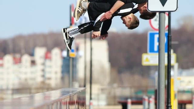 Two young men doing acrobatic parkour tricks with somersault in the end