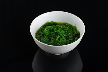Salad with seaweed and sesame in the dark plate in the center of the black background.