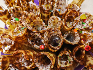 Close-up of delicious chocolate waffle rolls lie on white plate. Preparation of a sweet dessert. White clean kitchen and table. Many wafer tubules are group. Edible tubes with white spiral from cream.
