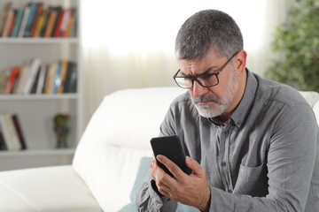 Confused adult man using a smart phone at home - obrazy, fototapety, plakaty