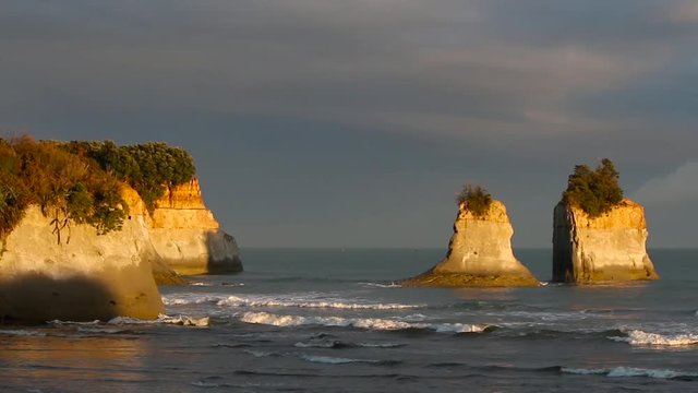 The dramatic first sunlight appears on sea stacks in front of a dark sea and sky. WIDE.