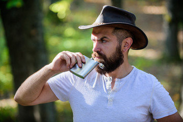Guy brutal bearded cowboy drink alcohol metal flask. Hipster with beard drink alcohol nature...