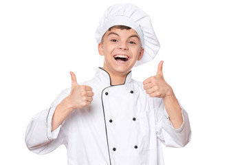 Handsome teen boy wearing chef uniform making thumbs up gesture. Portrait of a happy cute male child cook, isolated on white background. Food and cooking concept.