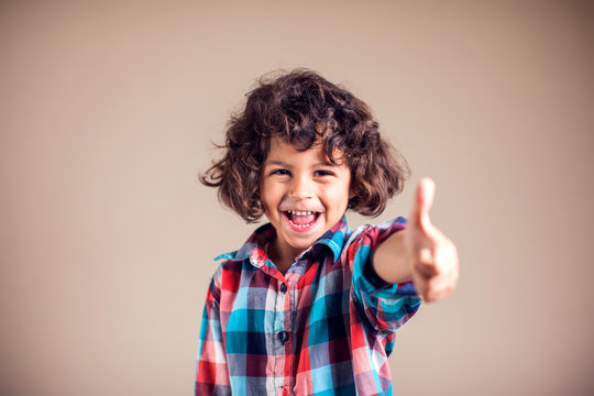 Little cute boy on grey background shows tumbs up gesture.. Children and emotions concept