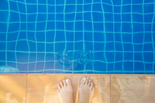 Top view of bare female foot standing beside the edge of blue swimming pool with wave on the sunny day
