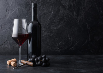 Elegant glass and bottle of red wine with corks and corkscrew on black stone background. Natural...