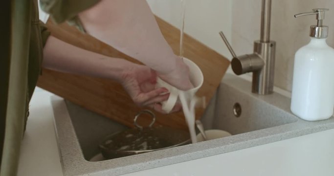 Woman washing dishes in the sink in the kitchen. In her hands she has a white mug and a sponge with which she washes. After washing the mug, she puts it on the table.