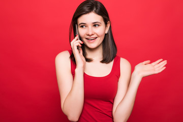 Photo of young shocked lady standing isolated over red background talking by mobile phone.
