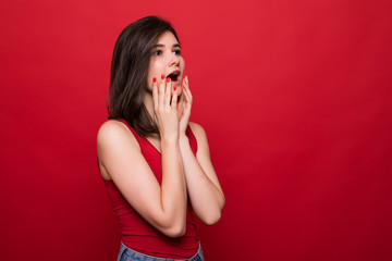 Portrait of happy surprised young woman standing isolated over red background.