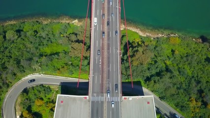 Aerial, tilt up, drone shot, above the 25 of April or the Salazar bridge and road A2, full of cars and trucks, revealing the coast of Lisboa city, on Tejo river, in Lisbon, Portugal