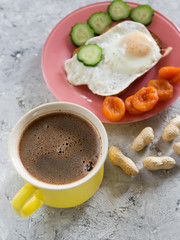 Sandwich with fried egg, nuts, dried apricots and cucumber and a Cup of coffee on a concrete background