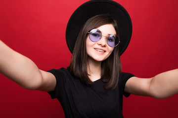 Fashion hipster woman taking selfie. Black hat, leather jacket, sunglases, bright red lips. Trendy fashion style