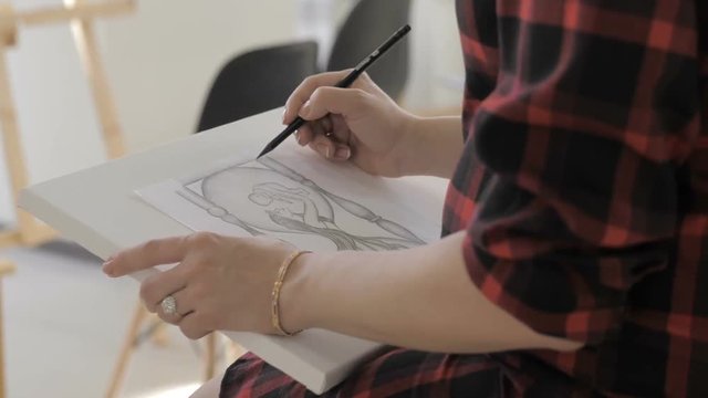 The girl's hand draws a picture with a pencil on white paper