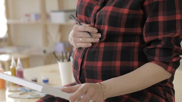 Young pregnant woman drawing painting in art studio, healthy happy lifestyle concept