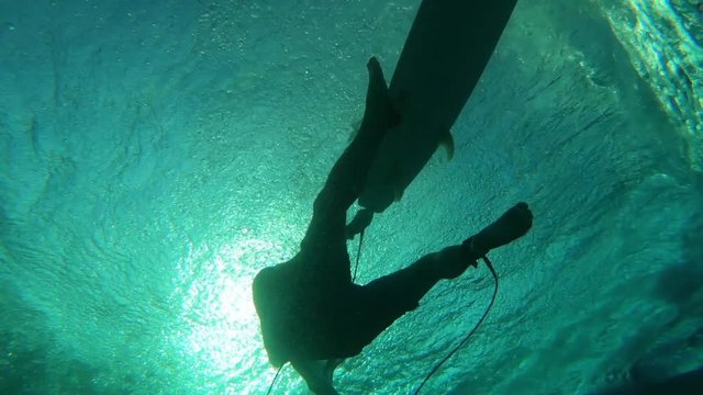 Underwater view of the surfer floating on the surface with surfboard and passing the wave