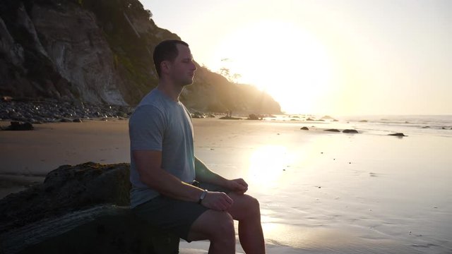 A strong young man in silhouette sitting in a meditation pose to release stress and train mindfulness and positivity at sunrise in Santa Barbara, California SLOW MOTION.