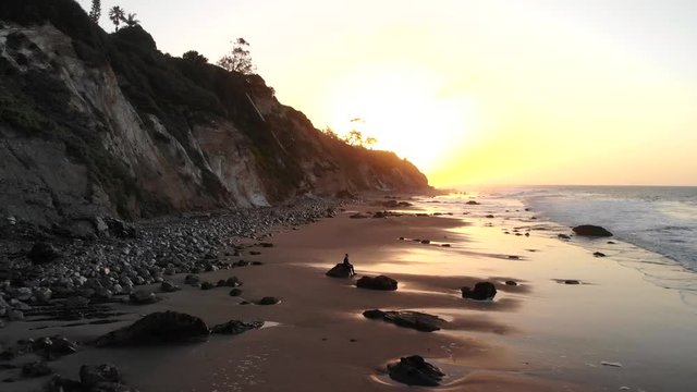 A man in silhouette sitting in a peaceful meditation pose to practice mindfulness on the calming sandy beach at sunrise in Santa Barbara, California