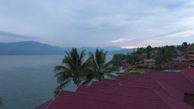 Drone footage of a woman walking across a tiled roof at sunrise at a waterfront resort on Lake Toba in North Sumatra, Indonesia. Series 1.