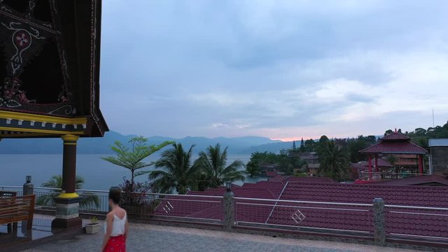 Drone footage of a woman walking across a tiled roof at sunrise at a waterfront resort on Lake Toba in North Sumatra, Indonesia. Series 2.