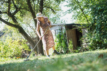 Senior woman raking up the leaves in a garden, Altötting, Bavaria, Germany