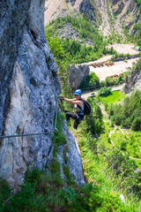 Female climber hanging from a via ferrata cable on "Astragalus" route, a popular tourist attraction in Bicaz Gorge (Cheile Bicazului), Neamt county, Romania. Aerial view from high above on a mountain.