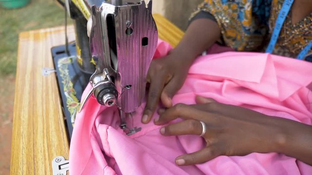 Close up slow motion shot from above of an African womans hands as she sews clothing with a tailoring machine.