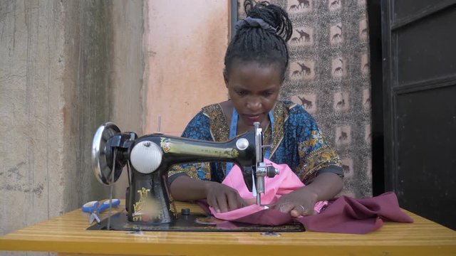 Front shot of an African woman sewing cloths on a tailoring machine in Africa outside her small home.
