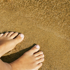 Teen girl's bare feet standing on the sand of a lake beach near the water on summer vacations. Concept of a rest on the beach in summer heat