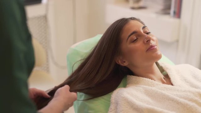 Caucasian Female Laying on Bed in Bathrobe While Mesotherapy Specialist Taking Care of Her Hair. Light Camera Movement