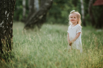 Beautiful baby girl walking in a sunny garden with a basket. little girl in a white dress with a basket in the park