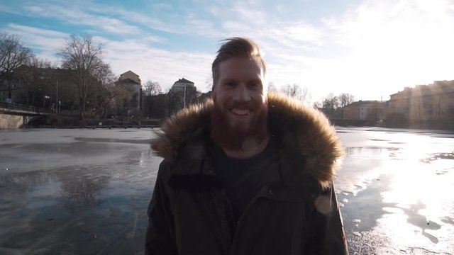 Handsome happy bearded hipster guy looking straight into the camera. Backlit Steadicam footage slow motion. Caucasian male full beard outside on a cold winter day.