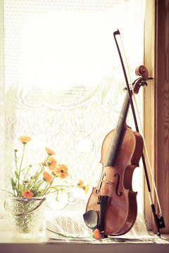 Vertical image of flowers and violin with sheet music  the front of the fiddle on windows background.
