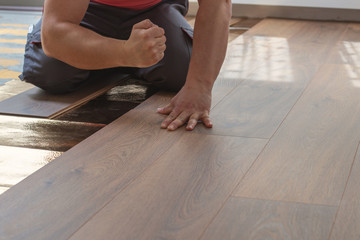 hands of handyman beat the laminate plank to laying the laminate floor