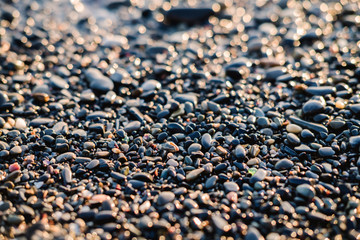 Small stones by the sea with bokeh effect. Blurred decorative vacation and holiday background, place for text. Summer wallpaper, sunny sunset light.