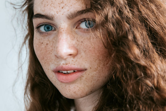Beautiful Freckles young woman close up portrait. Attractive model with beautiful blue eyes and ginger curly hair