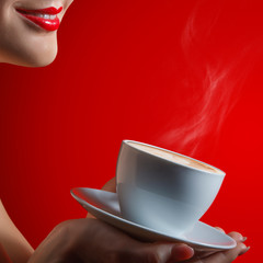 Womans smile lips and cup with coffee cappuccino in hand in studio at the red background, close up