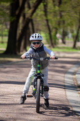 Naklejka premium Little boy learns to ride a bike in the park. Cute boy in sunglasses rides a bike. Happy smiling child in helmet riding a cycling.