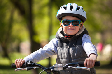 Little boy learns to ride a bike in the park. Cute boy in sunglasses rides a bike. Happy smiling...