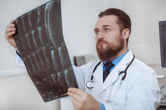 Close up of a handsome bearded male doctor examining x-ray scans of a patient. Focused male medical worker looking at mri scans of a patient. Profession, health care concept