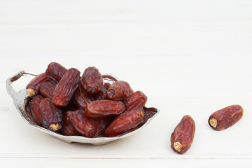 Islamic festival of Ramadan concept. with a delicious tropical dates on a silver plate and shiny rosary on a white wooden table background. Traditional Middle East culture. Ramadan Kareem.