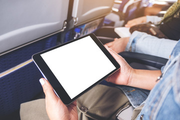 Mockup image of a woman holding and looking at black tablet pc with blank white desktop screen while sitting in the cabin